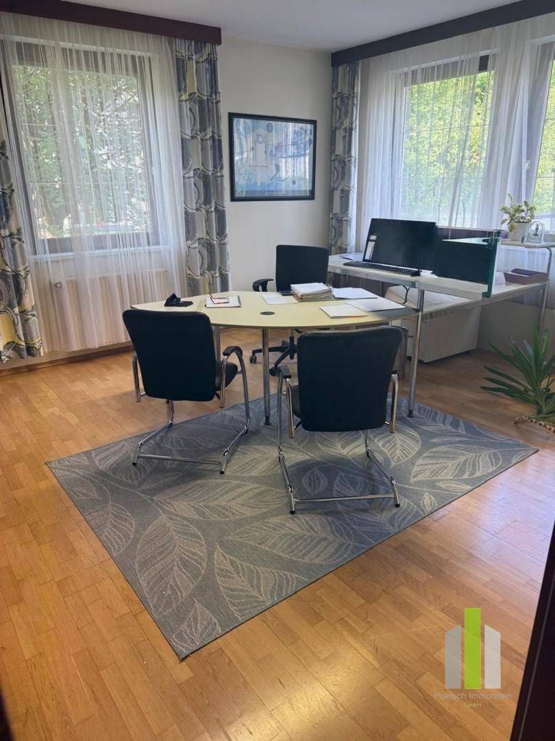Helles Büro mit Holzboden, großen Fenstern und einem modernen Schreibtisch.