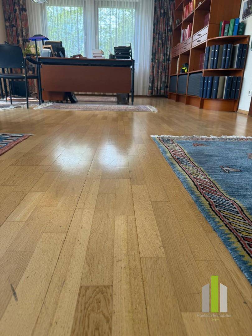 Detailaufnahme des Holzboden in einem Büro mit Teppichen und Bücherregal im Hintergrund.