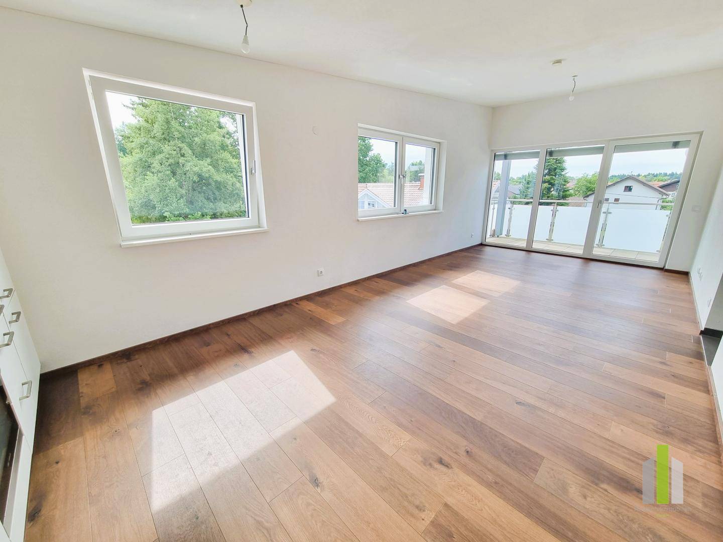 Geräumiges, helles Zimmer mit Holzboden und Zugang zu einem Balkon, ideal als Wohnbereich.
