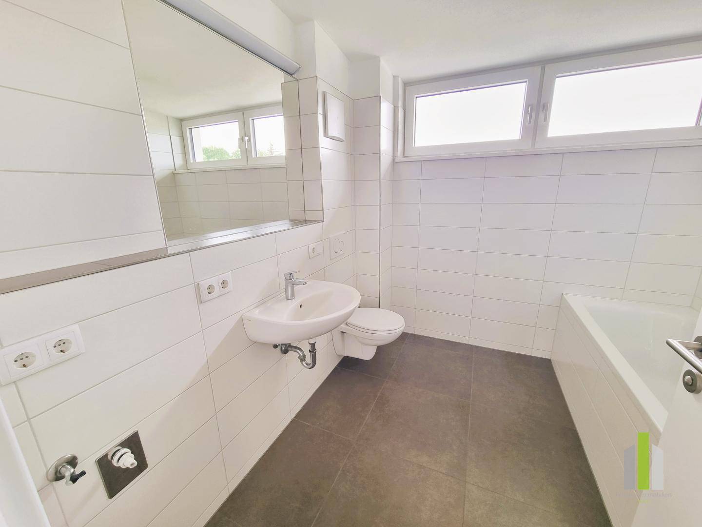 Modernes Badezimmer mit weißen Fliesen, Waschbecken, Toilette, Badewanne und Fenster.