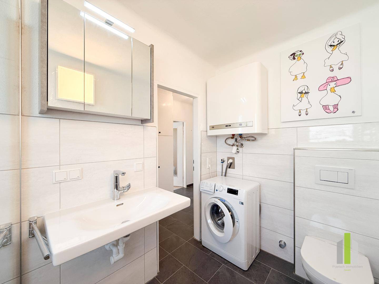 Helles Badezimmer mit WC, Waschbecken, Spiegelschrank und integrierter Waschmaschine.