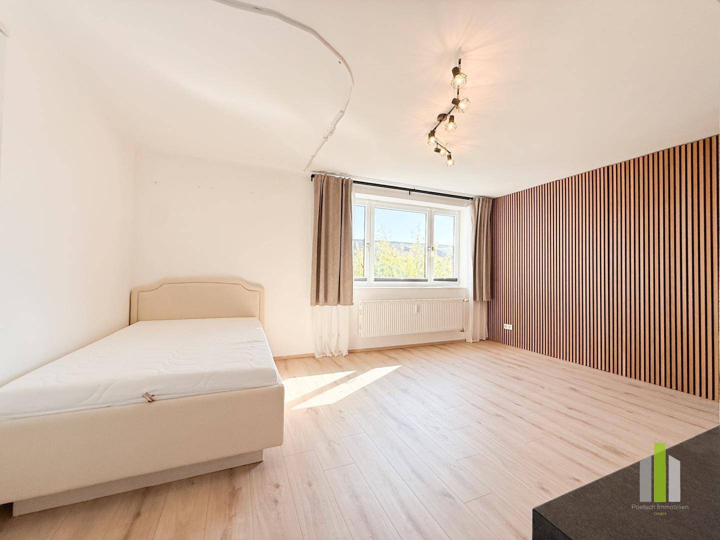 Gemütliches Schlafzimmer mit Einzelbett, großen Fenstern und stilvoller Holzlattenwand.
