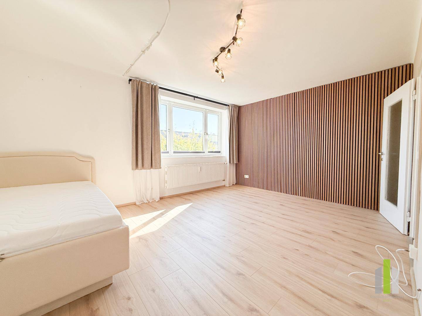 Geräumiges Schlafzimmer mit heller Einrichtung, dekorativer Holzlattenwand und viel Tageslicht.