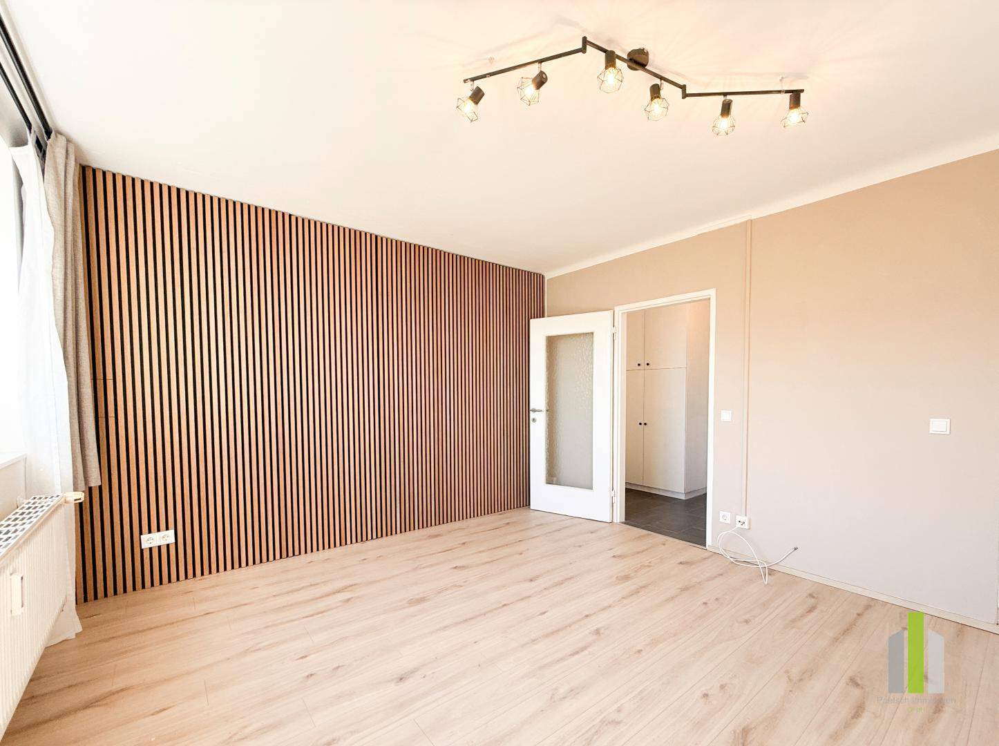 Heller Wohnbereich mit moderner Holzlattenwand, hellem Laminatboden und Zugang zu einem Nebenraum.