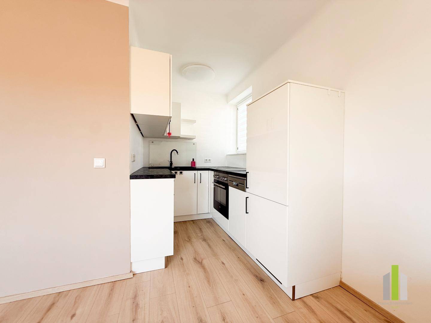 Kompakte Einbauküche mit weißen Schränken, dunkler Arbeitsplatte und integriertem Backofen, ideal für kleine Wohnungen.
