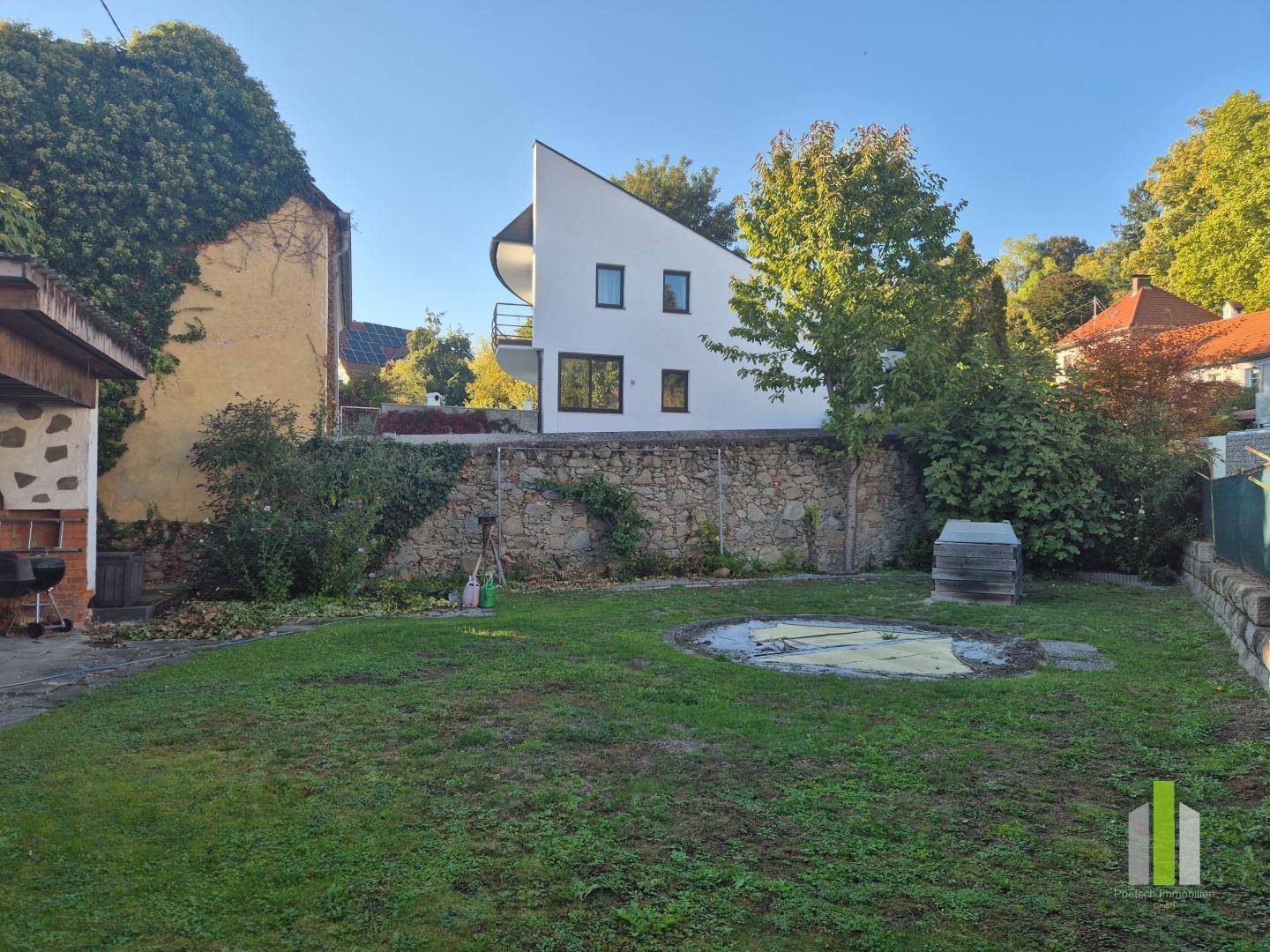 Grüner Garten mit Rasenfläche und einem modernen Haus im Hintergrund unter blauem Himmel.