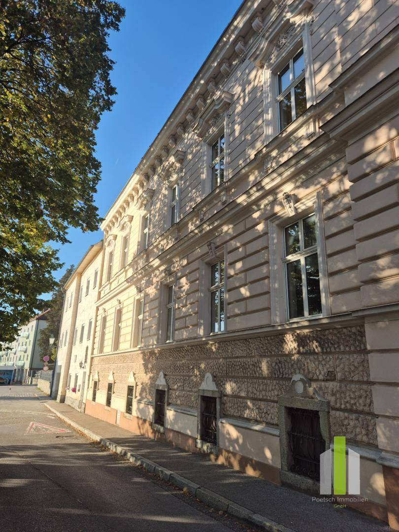 Lange Fassade eines historischen Gebäudes mit vielen Fenstern entlang einer ruhigen Straße.