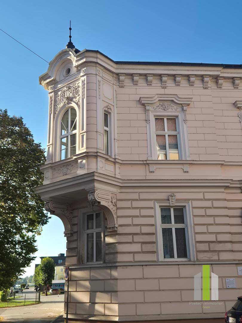 Historisches Eckgebäude mit markantem Erker und dekorativen Elementen unter blauem Himmel.