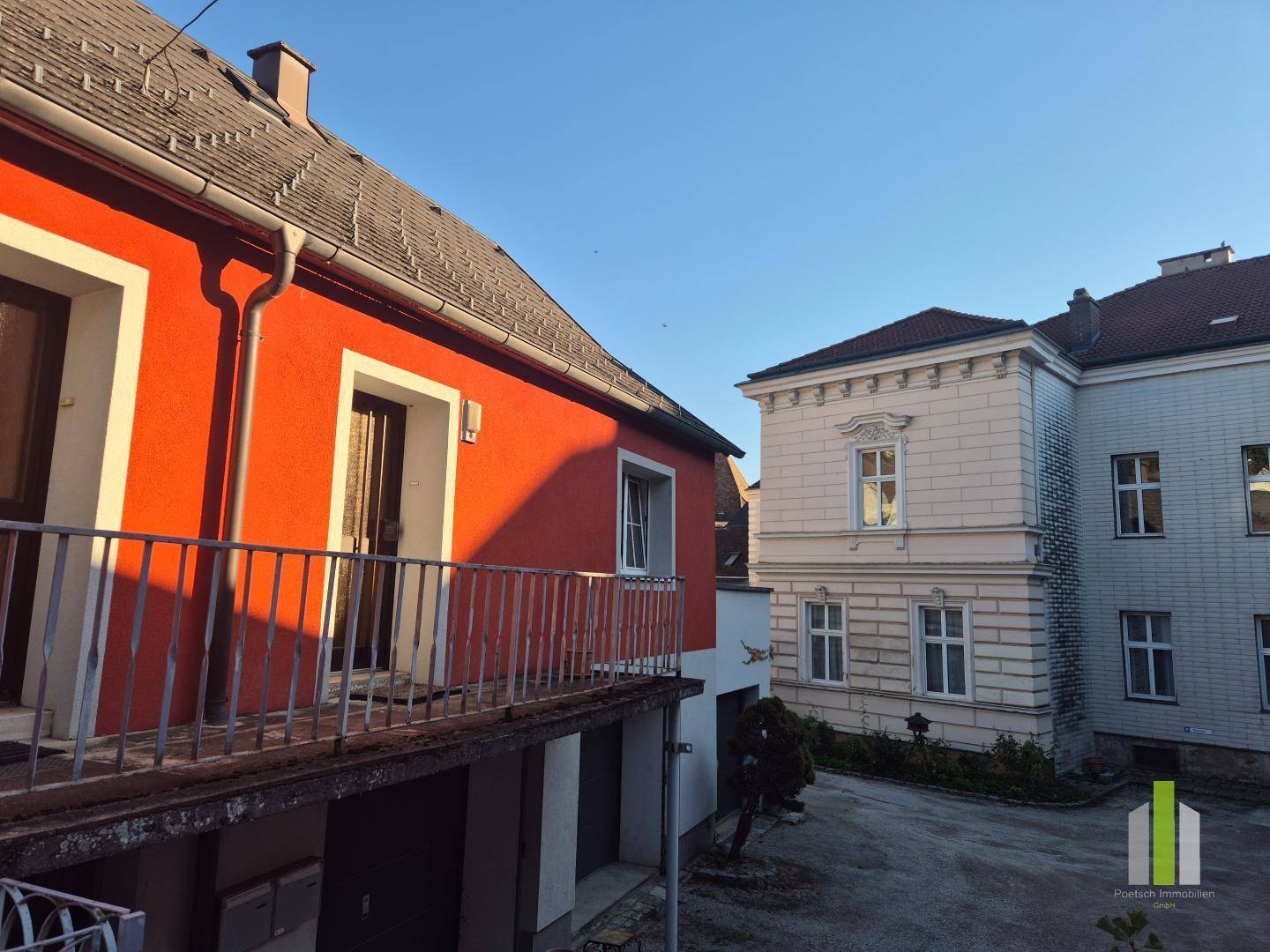Blick von einem Balkon auf ein rotes Gebäude und ein historisches Nachbargebäude.