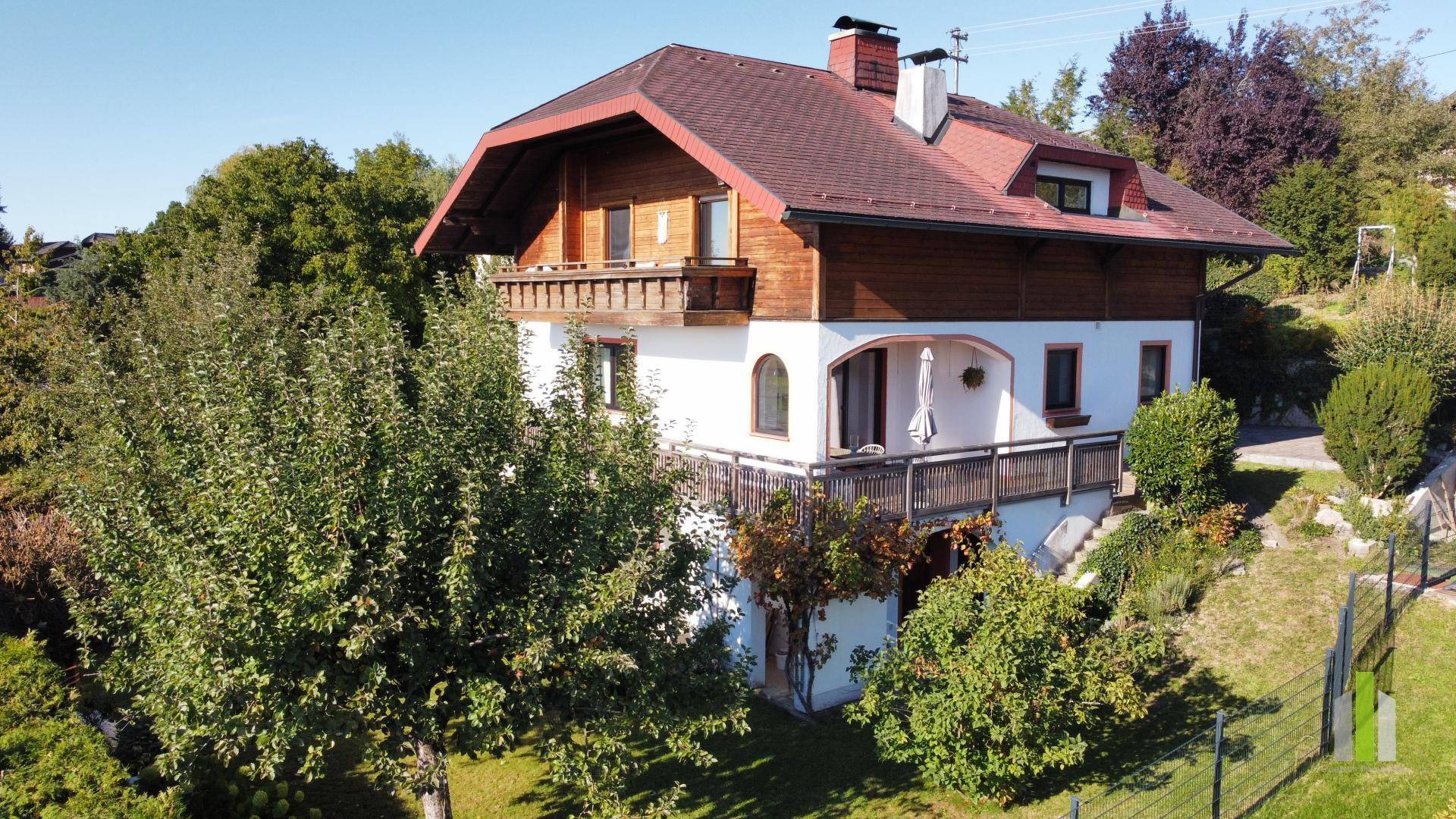 Charmantes Landhaus mit mehreren Balkonen, Holzgeländern und umgebender Grünfläche.