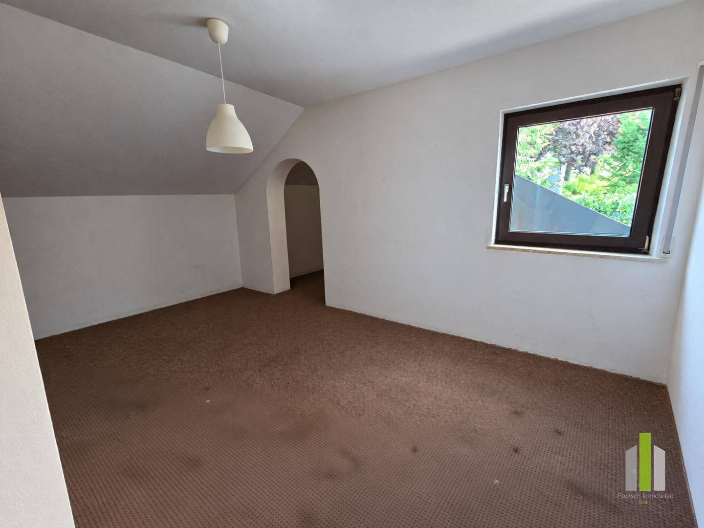 Geräumiges Zimmer mit Dachschräge, Teppichboden und einem Fenster mit Blick nach draußen.