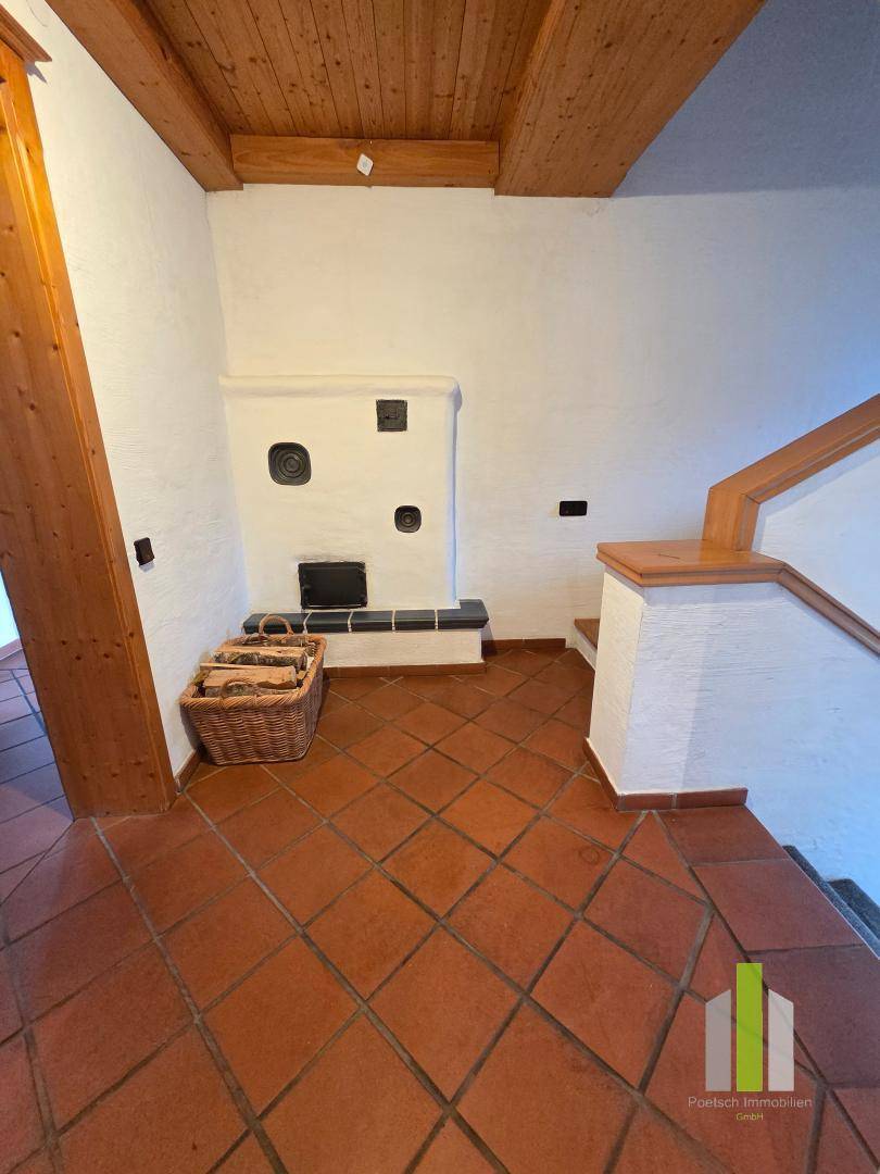 Eingangsbereich mit Terrakottafliesen, Holztreppe und einem traditionellen Kachelofen.