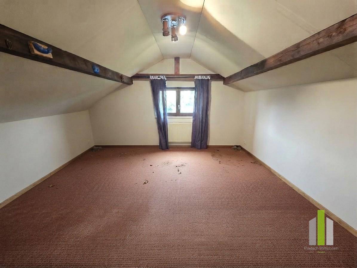 Dachbodenraum mit sichtbaren Holzbalken, Teppichboden und einem Fenster.