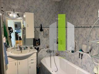 Badezimmer mit Badewanne, Waschbecken und hellgrauen Fliesen im 80er-Jahre-Stil.