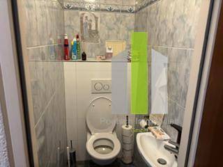 Separates WC mit Toilette, kleinem Waschbecken und hellgrauen Wandfliesen.