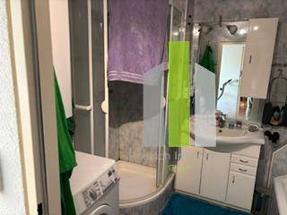 Badezimmer mit Duschkabine, Waschbecken und Waschmaschine, gefliest in hellem Grau.