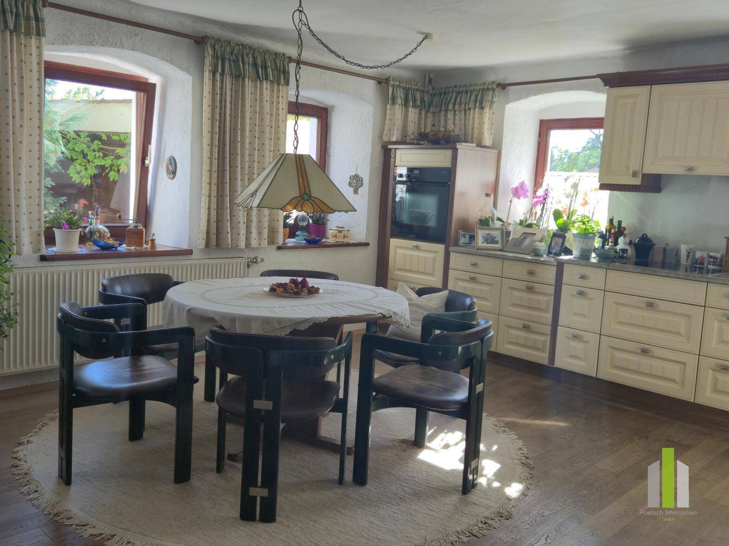 Gemütliche Landhausküche mit Essbereich, Holzboden und traditionellen Möbeln unter Bogenfenstern.