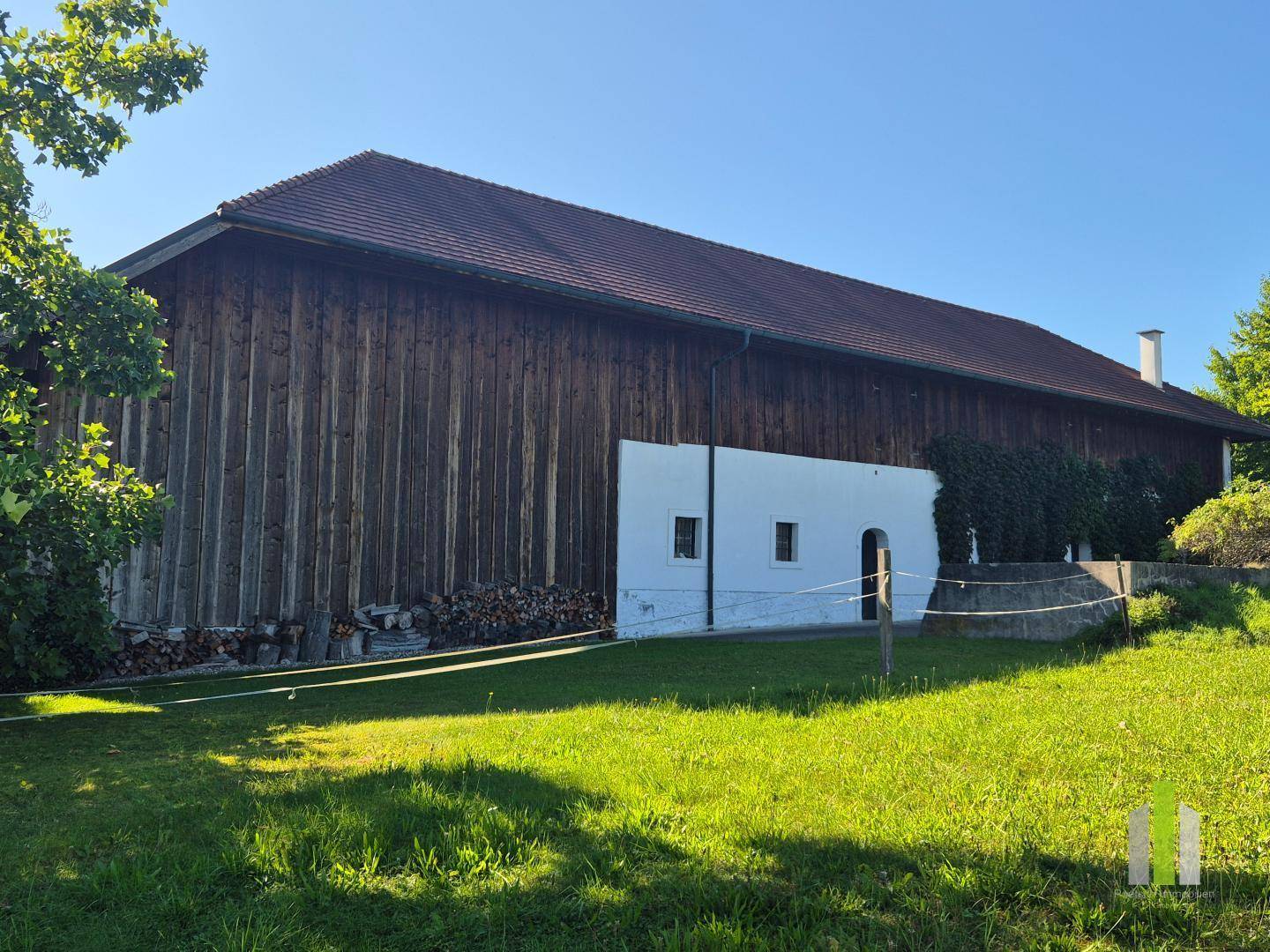 Großes Holzgebäude mit rotem Dach und angrenzender Wiese unter blauem Himmel, ländliche Idylle.