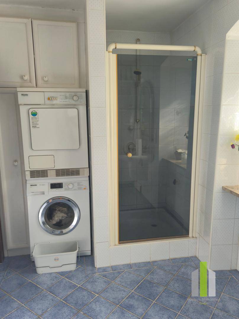 Badezimmer mit Duschkabine, Waschmaschine und Trockner, umgeben von weißen Fliesen.