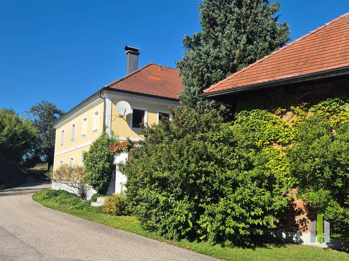 Gelbes Landhaus und Nebengebäude mit üppiger Vegetation, verbunden durch eine Zufahrt.