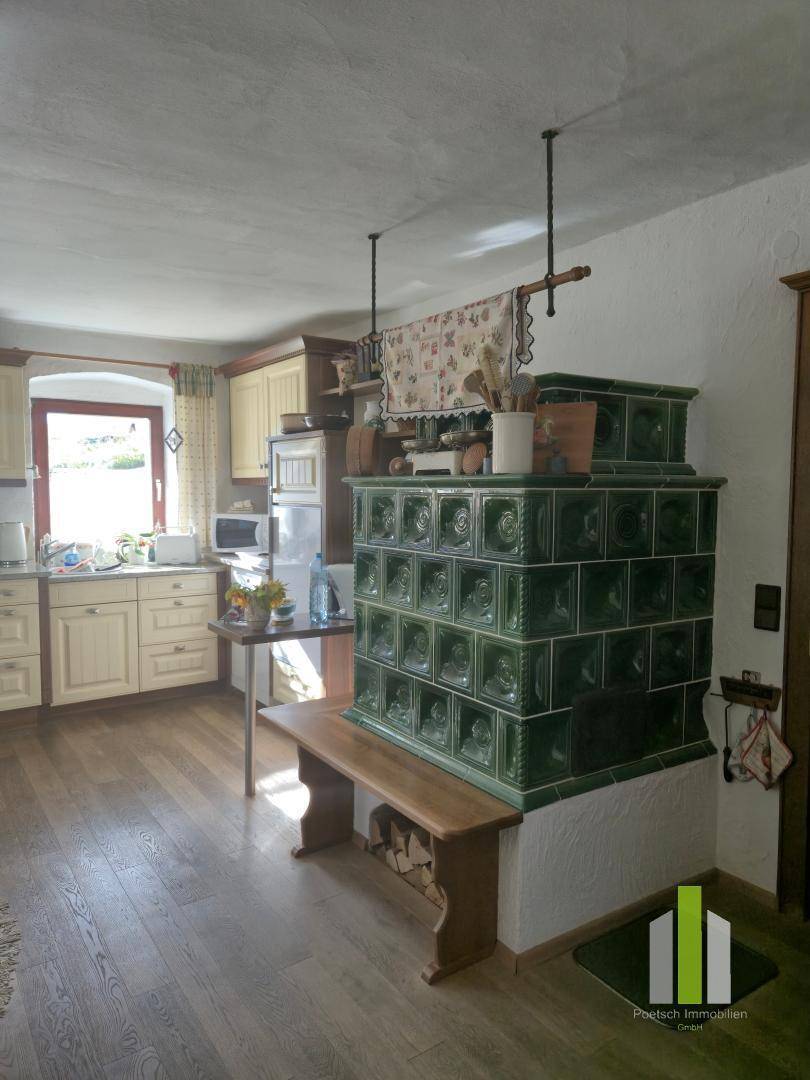 Traditionelle Küche mit grünem Kachelofen, Holzboden und Einbauküche im Landhausstil.