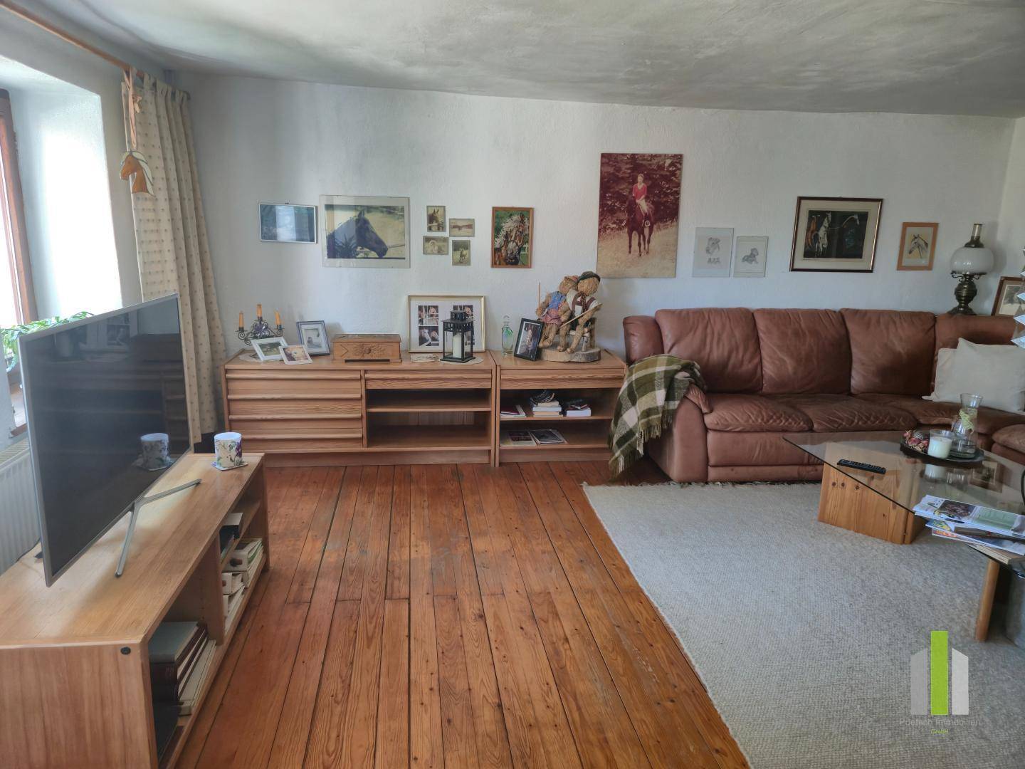 Gemütliches Wohnzimmer mit Holzdielenboden, Ledersofa und rustikalen Holzmöbeln, gut beleuchtet.