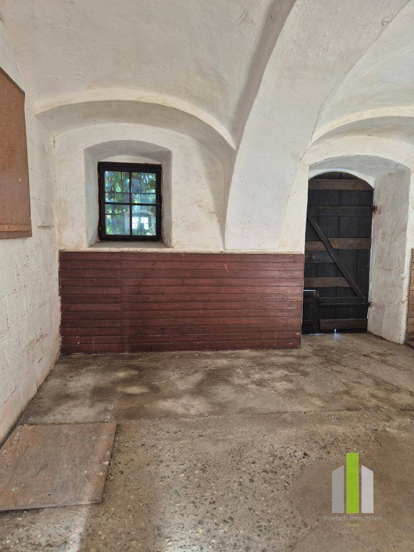 Leerer Stallbereich mit Holzwänden, gewölbter Decke und kleinem Fenster, gut erhalten.