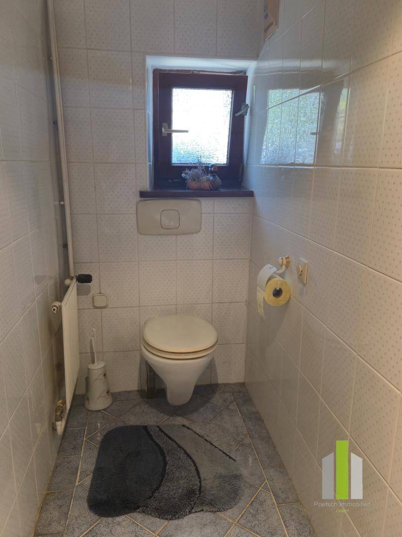 Separate Toilette mit Fenster, weißen Fliesen und Heizkörper.