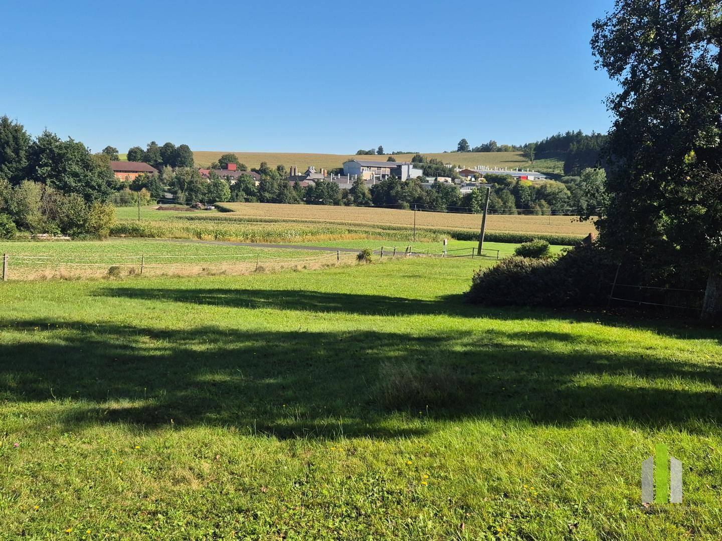 Panoramablick über grüne Felder und eine ländliche Siedlung unter blauem Himmel.