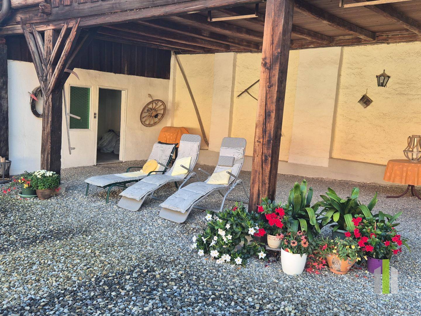 Gemütlicher überdachter Bereich im Innenhof mit Liegestühlen und bunten Topfpflanzen. 