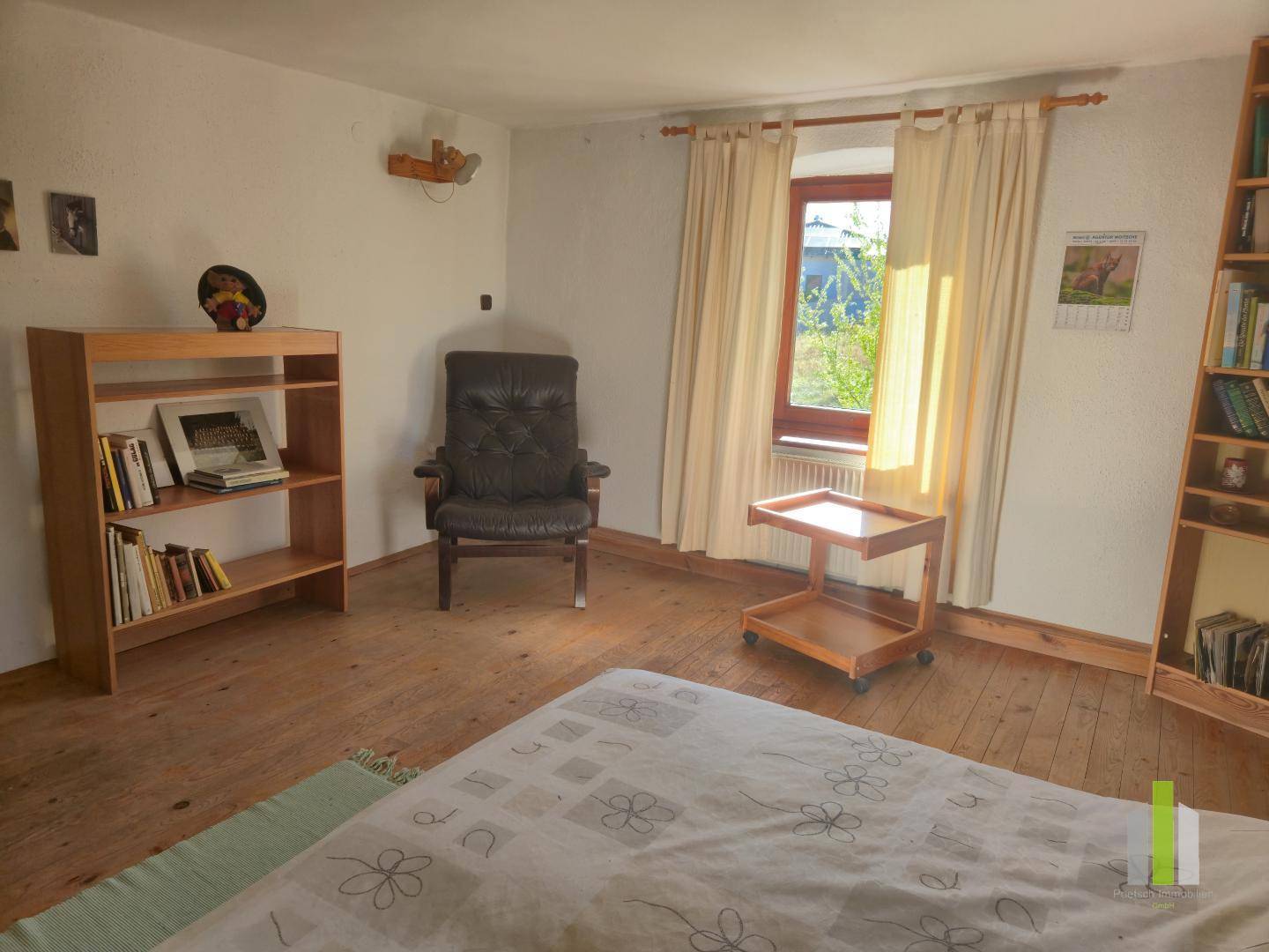 Helles Schlafzimmer mit Holzboden, Sessel und Bücherregalen.