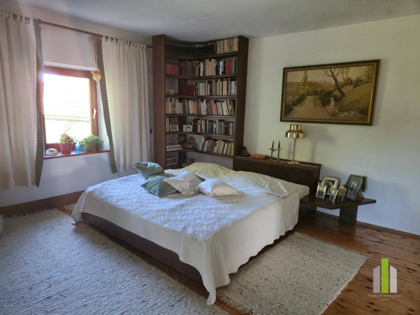 Schlafzimmer mit Holzdielenboden, großem Bett, Teppich und einem Bücherregal, hell und einladend.