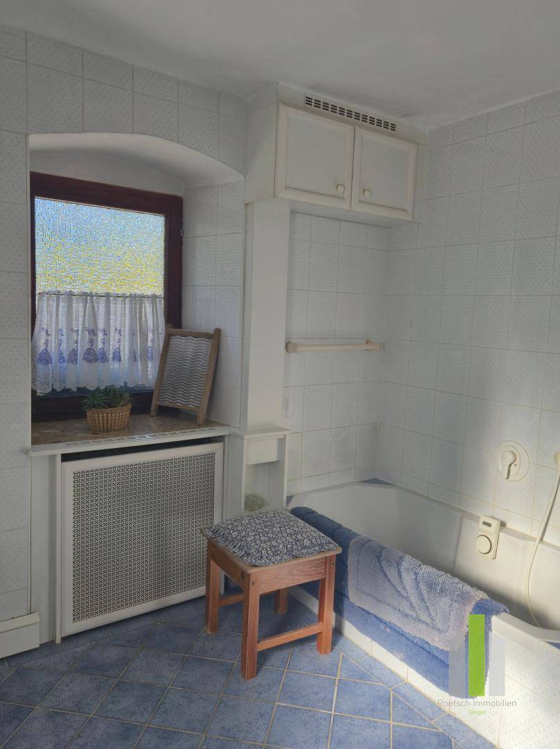 Badezimmer mit Badewanne, blauen Fliesen und Fenster, ausgestattet mit einem Heizkörper.