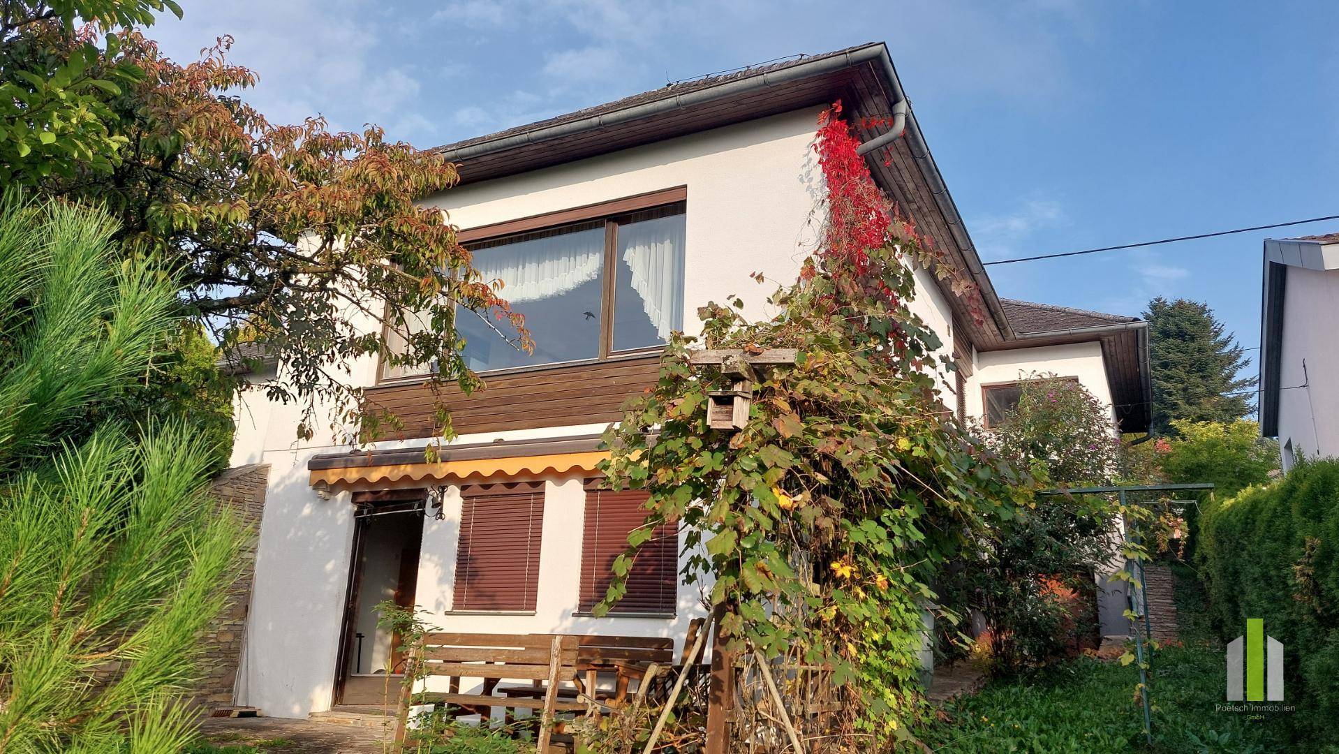 Ansicht des Hauses von der Seite, umgeben von Bäumen und Kletterpflanzen.