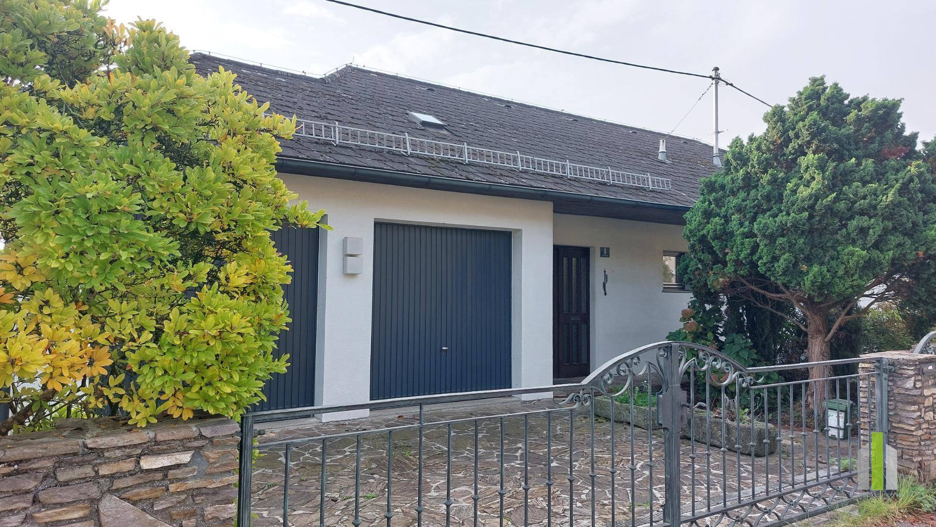 Vorderansicht des Hauses mit Garagentor, schmiedeeisernem Tor und Steinmauer.