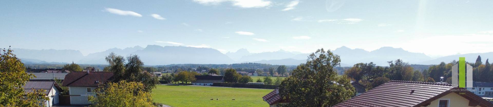 Panoramablick auf eine weite Landschaft mit Feldern, Häusern und einer beeindruckenden Bergkulisse.