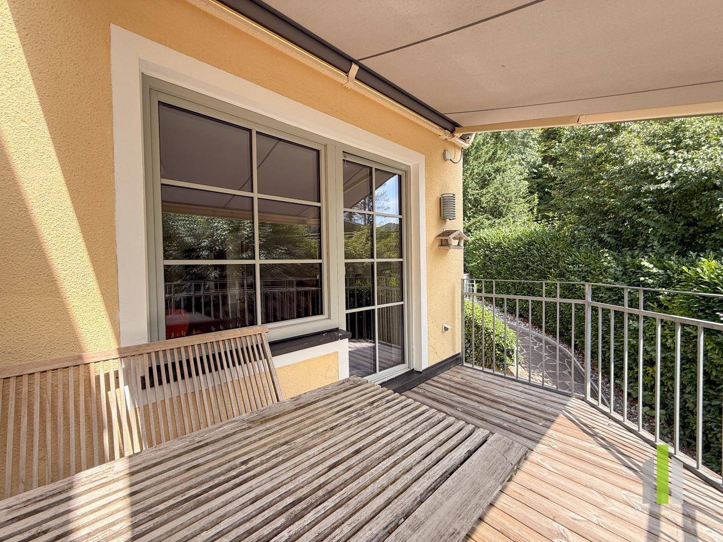 Überdachter Balkon mit Holztisch und Blick auf die grüne Umgebung, ideal für Entspannung.