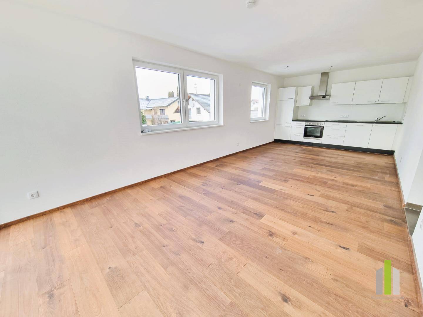Offener Wohnbereich mit integrierter, moderner Einbauküche und hellem Holzboden.