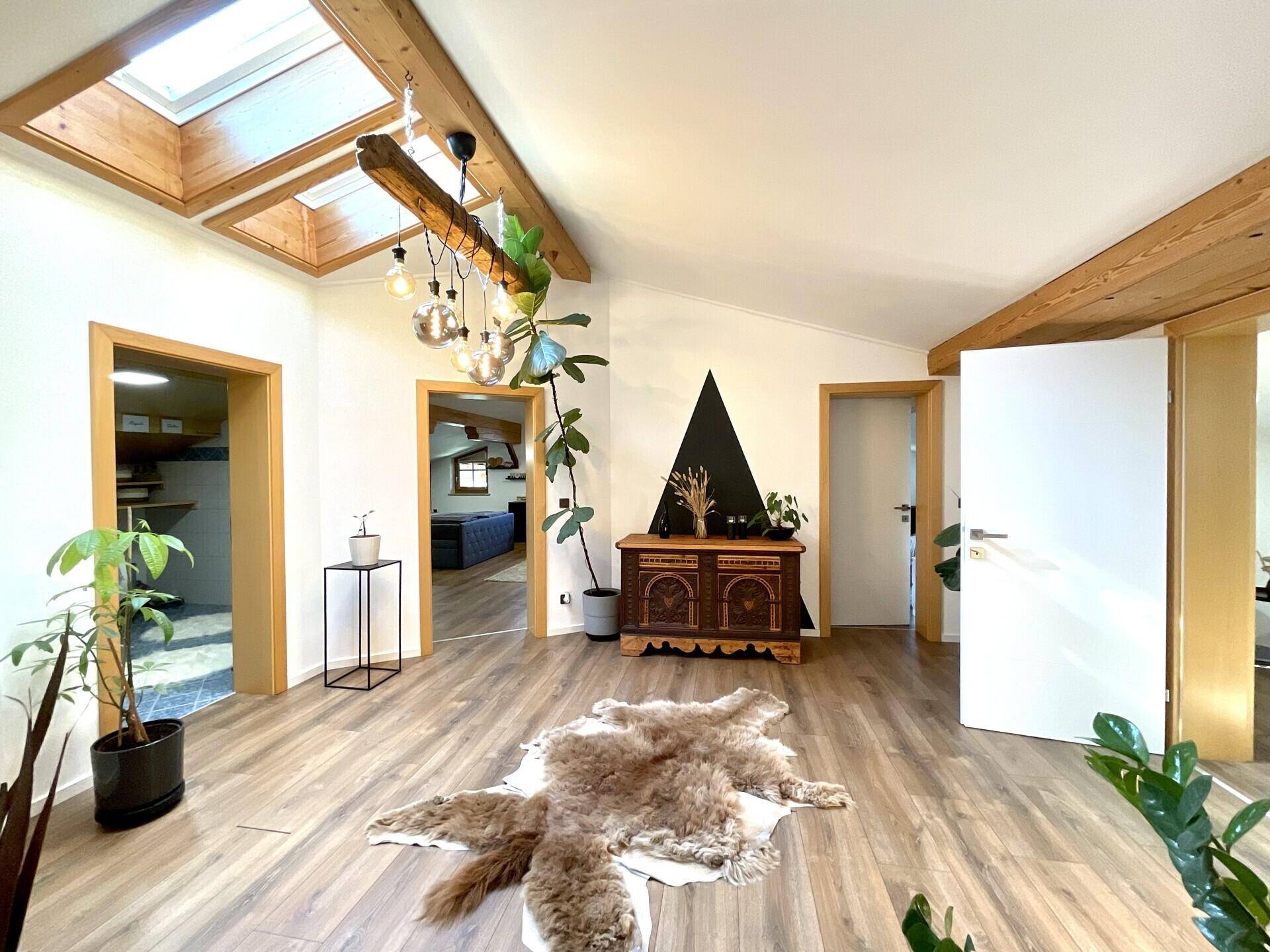 Heller Flur mit Holzbalken, Dachfenstern und modernem Laminatboden, geschmückt mit Pflanzen.