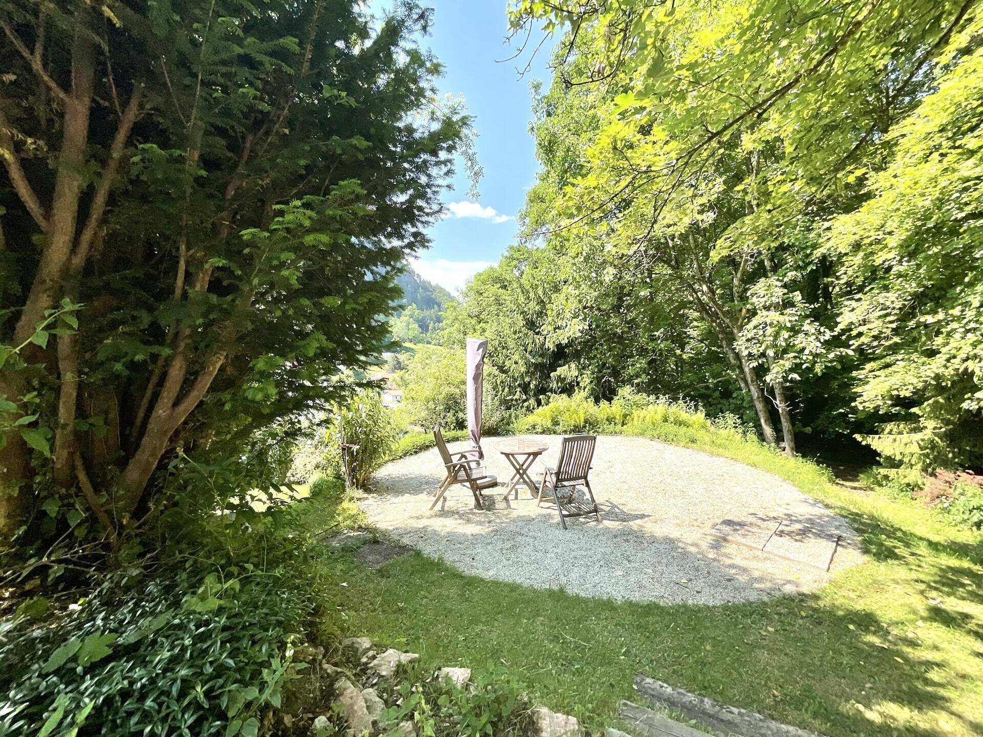 Ruhige Sitzecke im Garten umgeben von Bäumen mit Blick auf die Natur.