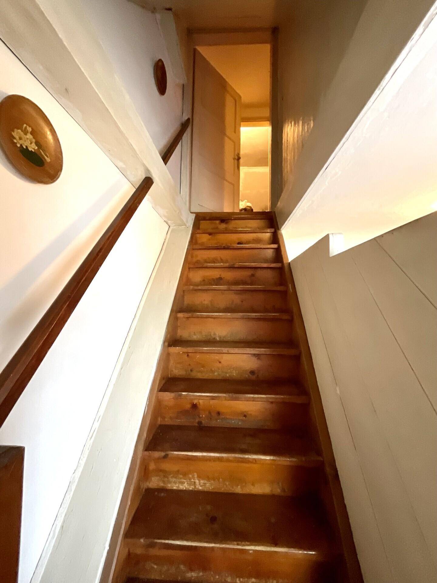 Rustikale Holztreppe mit weiß gestrichenen Wänden, die in ein Obergeschoss führt.