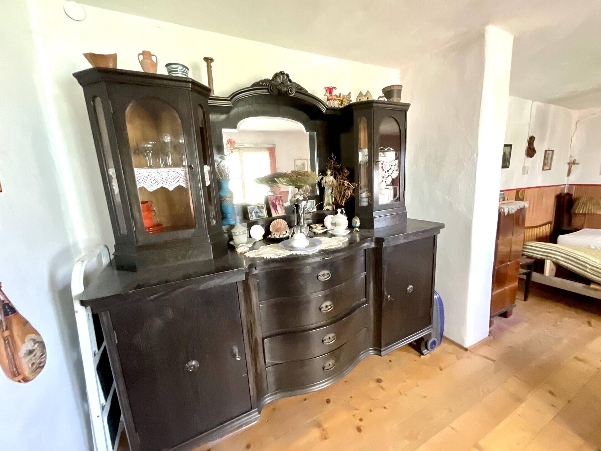 Antiker Holzschrank mit Spiegel und traditionellen Dekorationen in einem hellen Raum.