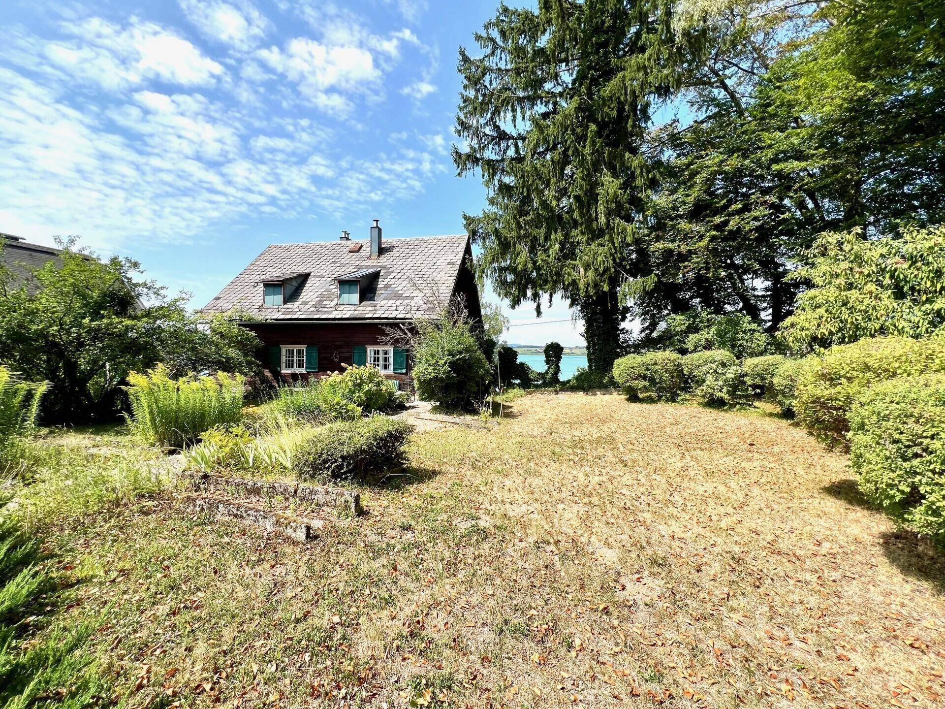 Charmantes Haus mit großem Garten und Blick auf den See unter blauem Himmel.