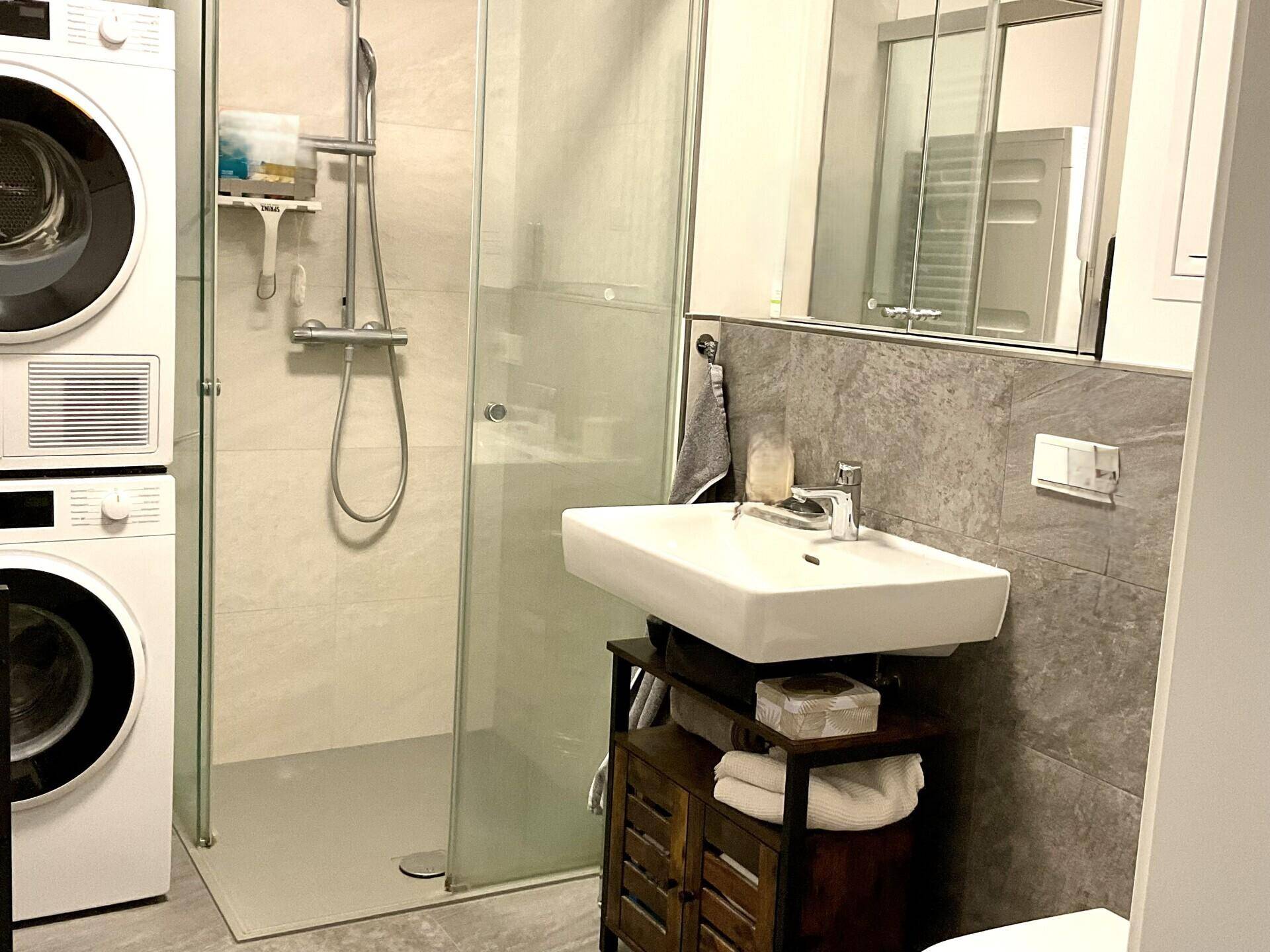 Modernes Badezimmer mit ebenerdiger Dusche, Waschbecken und Waschmaschine/Trockner-Turm.