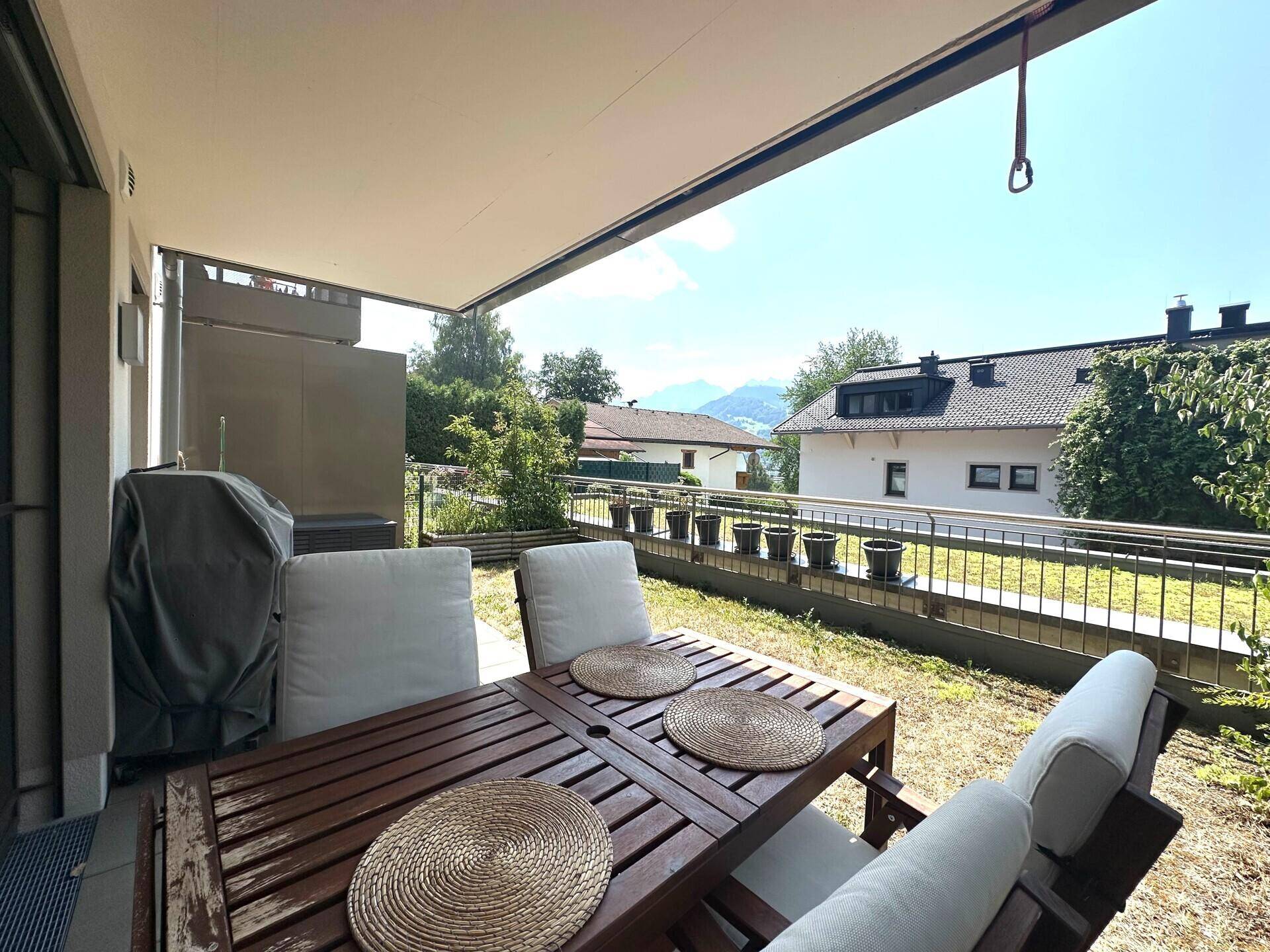 Sonnige Terrasse mit Holztisch, Gartenmöbeln und Blick auf die Umgebung.