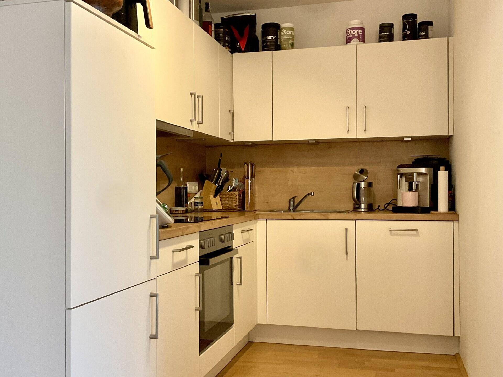 Kleine, funktionale Küche mit weißen Schränken, Holzarbeitsplatte und integriertem Backofen.