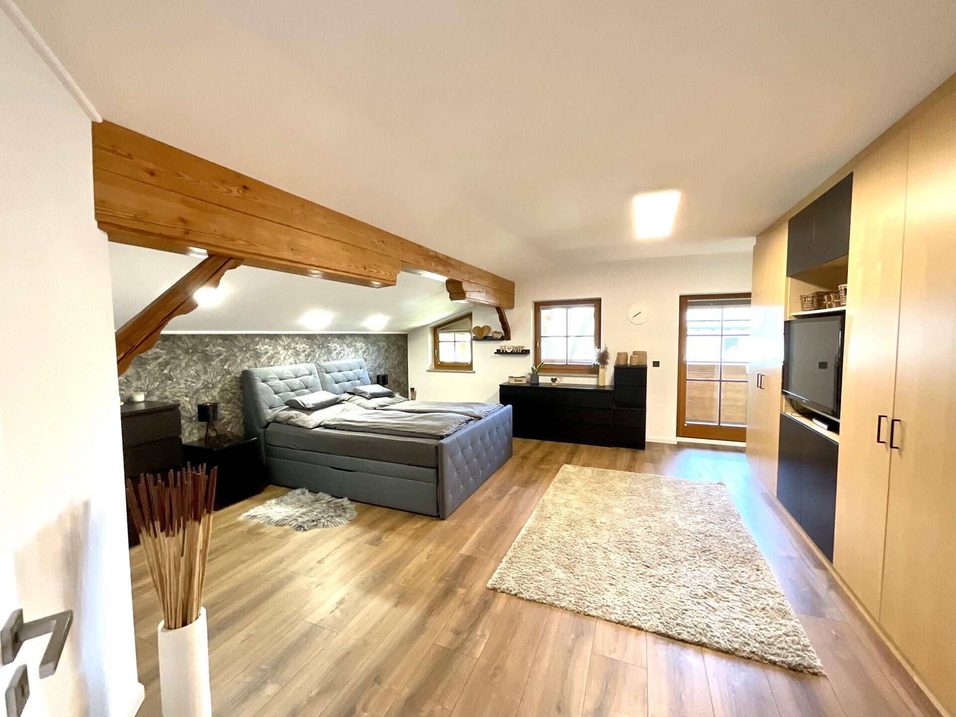 Gemütliches Schlafzimmer mit Holzbalken, Doppelbett und Einbauschränken unter Dachschrägen.