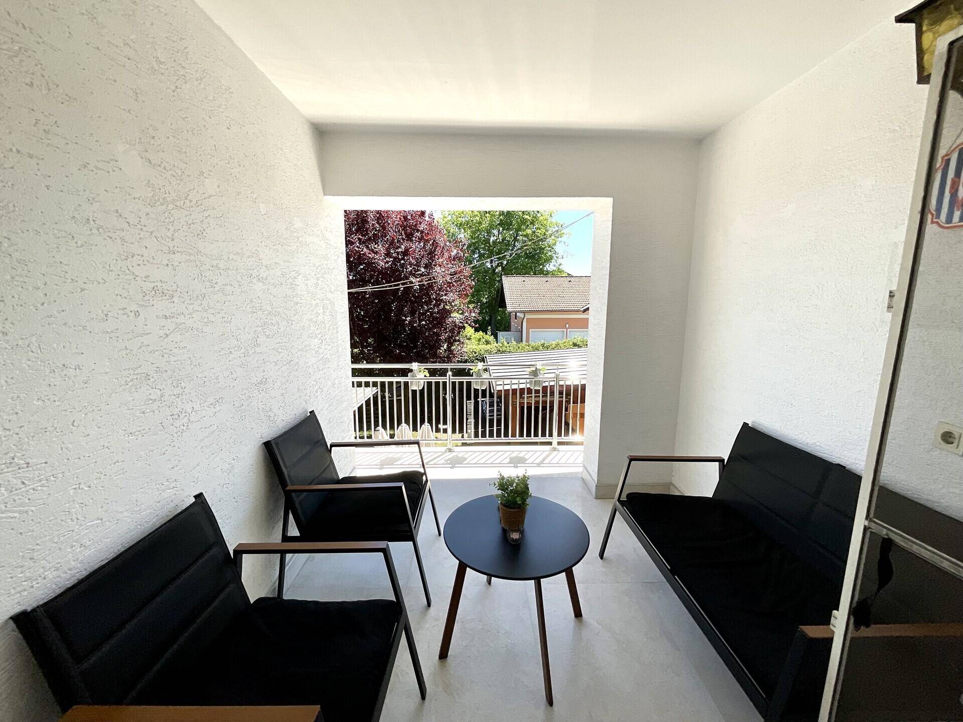 Gemütlicher Balkon mit modernen Sitzmöbeln und Blick ins Grüne an einem sonnigen Tag.
