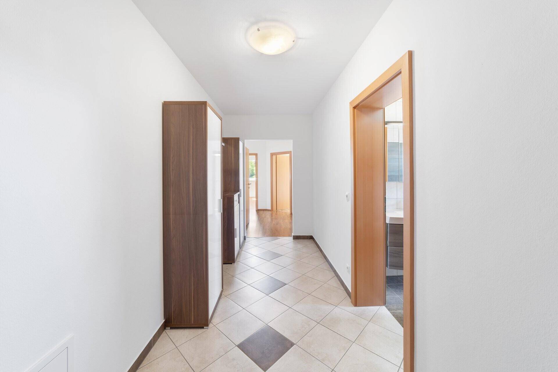 Heller Flur mit diagonal verlegten Fliesen und Holztüren, der zu weiteren Räumen führt.