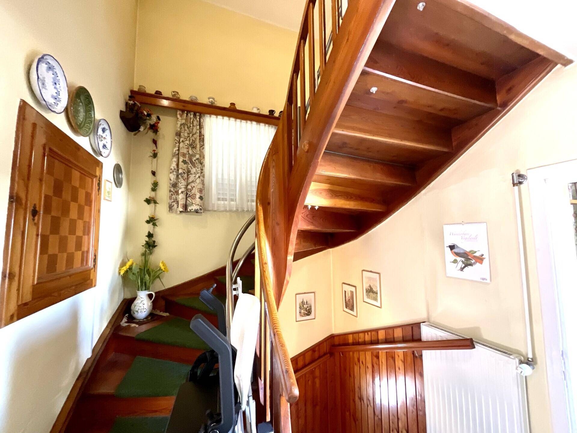 Traditionelles Treppenhaus mit Holzgeländer, gelben Wänden und natürlichem Licht.
